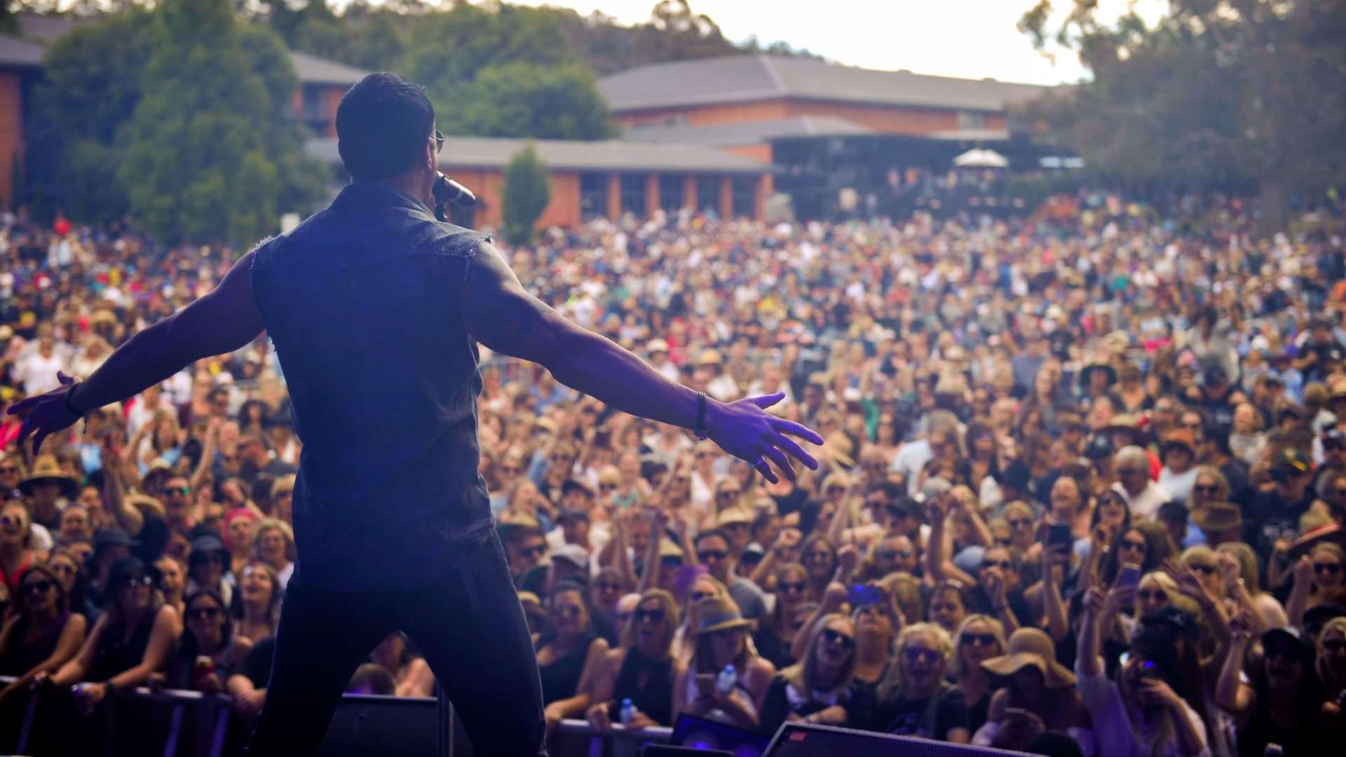 Photo taken from behind Rock singer Shannon Noll who is on stage performing to thousands of concert goers